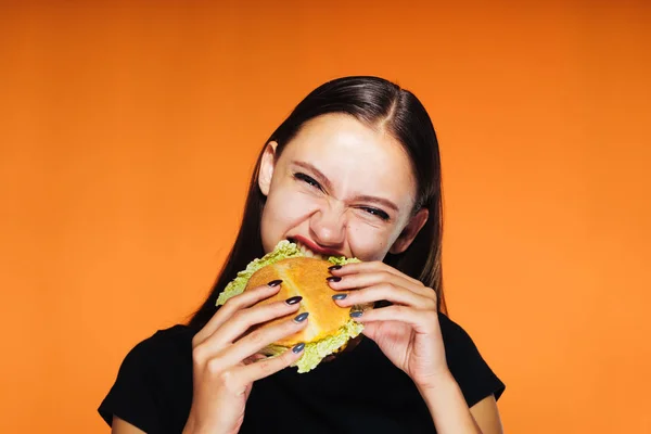 Hladová dívka sedí na dietu, ale jí nezdravé hamburger vysoce kalorické — Stock fotografie