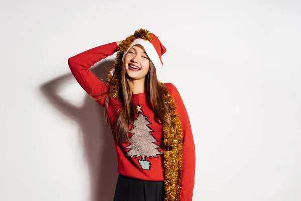 Una chica joven se ve feliz, celebra un nuevo año y la Navidad en una gorra roja y oropel de oro — Foto de Stock