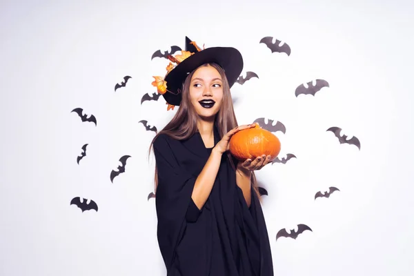 Breed Halloween party kunst design Halloween heks met een gesneden pompoen en in een zwarte verschrikkelijke hoed glimlacht. Tegen de achtergrond van een bos van vleermuizen. — Stockfoto