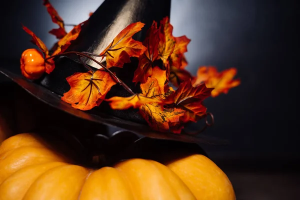 Grote pompoen voor halloween, zwarte heks hoed versierd met gouden herfst bladeren op een zwarte achtergrond — Stockfoto