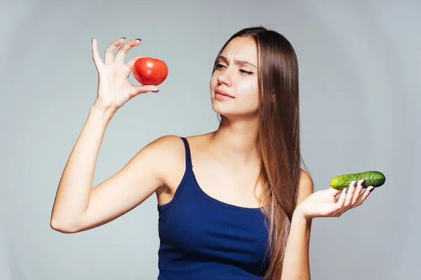 En flicka med en idrottsorganisation håller en gurka och en tomat. Flickan visar storleken på en tomat. Isolerade, hälsosam mat, rätt kost. — Stockfoto