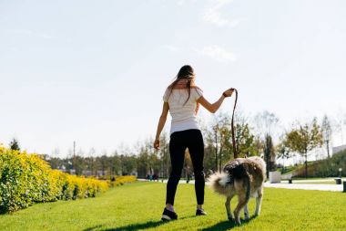genç kız bir beyaz T-shirt parkta yeşil çim üzerinde köpeğiyle yürüyor