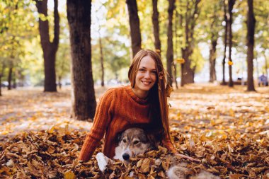 Kızıl saçlı gülen genç kız köpeğini ile düşen yapraklar parkta oturuyor