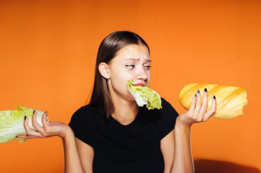 Kız bir lahana ve bir somun onun elinde tutar. Lahana, turuncu zemin üzerine izole çiğneme kız