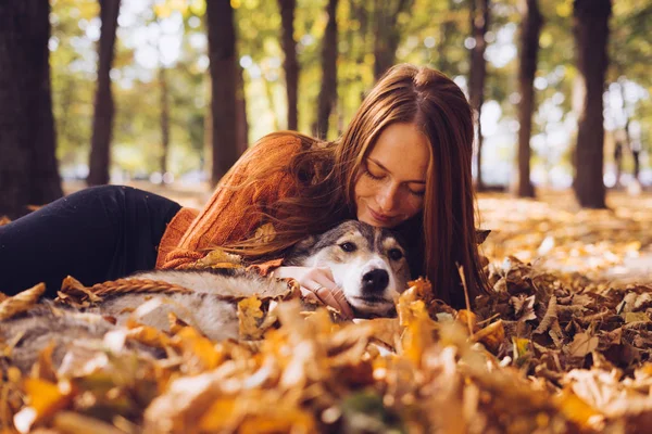 Rödhårig flicka ligger i fallna höstlöv med sin hund — Stockfoto