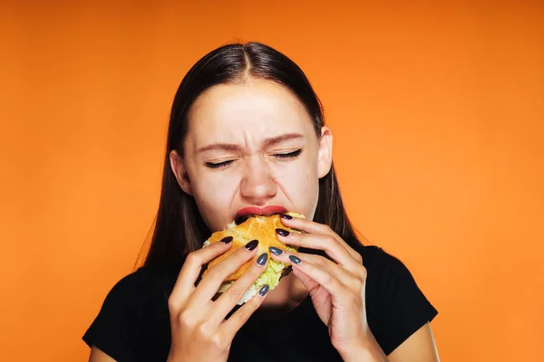 Dívka jí hltavě burger. chutné jídlo, izolované na oranžové pozadí — Stock fotografie