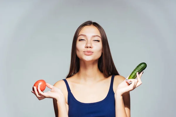 Das hübsche Mädchen im blauen T-Shirt verengte die Augen. Ein schönes Mädchen hält eine Gurke und eine Tomate in der Hand. isoliert auf weißem Hintergrund, gesund, gutes Essen — Stockfoto