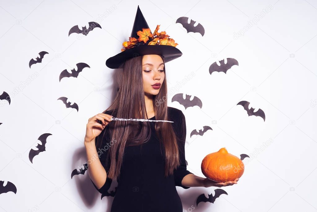 Gothic young girl in black, dressed up in halloween, holds a magic wand and conjures
