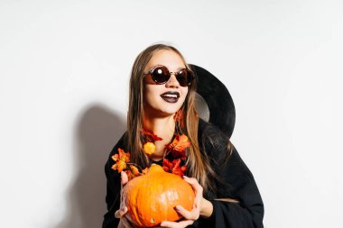 Halloween cadı bardaklarda ve kabak onun elinde tutan şapkasını çıkardı. Kabak tutan kostüm güzel genç kadın. 