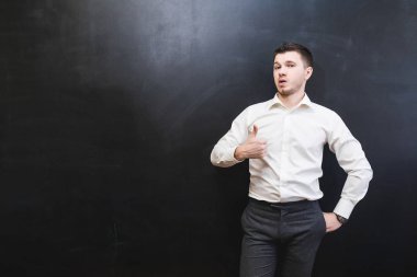 genç adam bir takım elbise içinde bir başparmak gösterilen siyah bir arka plan üzerinde duruyor