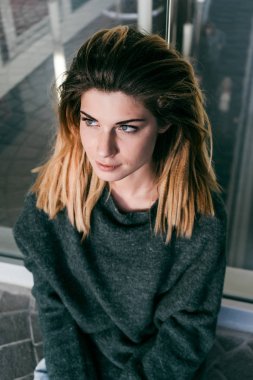 bir kız bir gri-yeşil kazaklı bir cam bina yakın oturur