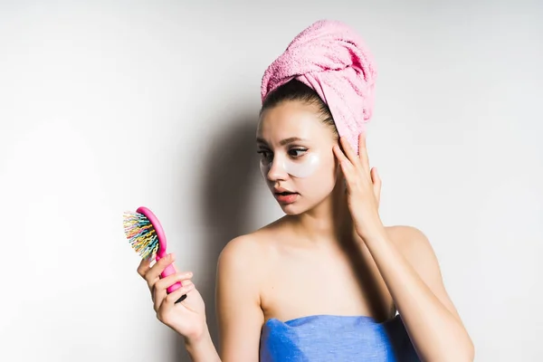 Девушка с полотенцем на голове с разочарованием смотрит на расческу в руке — стоковое фото