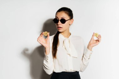 Modern başarılı genç iş kadını güneş gözlüklü bir altın bitcoin elinde tutar.