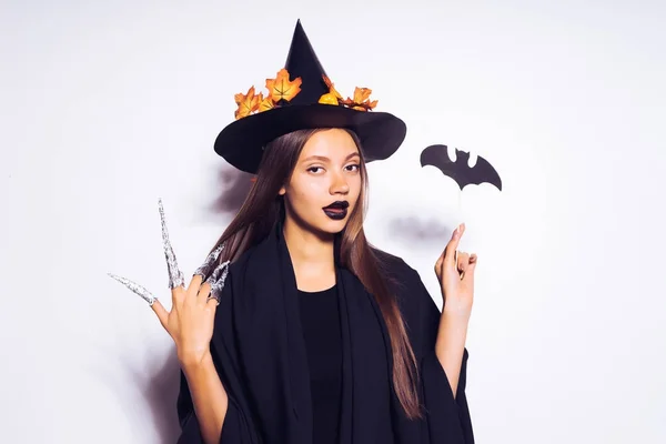 Una joven sexy misteriosa chica vestida con una bruja, celebra Halloween, en un gran sombrero negro, adornado con hojas amarillas —  Fotos de Stock
