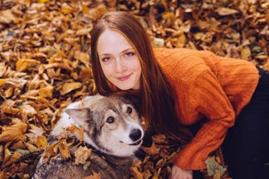 genç güzel kızıl saçlı kız parkta, onun köpek ile düşmüş sonbahar yığını içinde yürüyüş bırakır