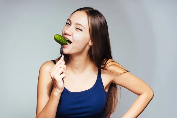 Egy fiatal sportos lány figyeli alakját, eszik egy alacsony kalóriatartalmú uborka — Stock Fotó