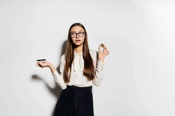 戴着眼镜的年轻成功的现代商业女人手里拿着一张银行卡和金比特币 — 图库照片