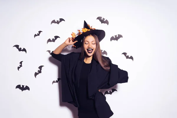 Joven chica gótica sexy en la forma de una bruja en Halloween, en un gran sombrero negro, posando contra la pared y riendo —  Fotos de Stock
