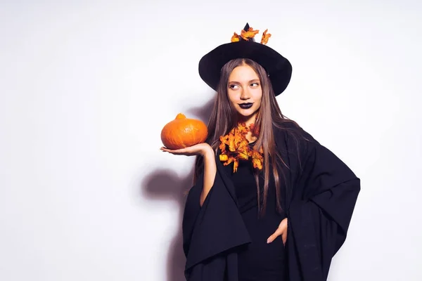 Young sexy gothic girl in the shape of a witch in halloween, in a big black hat, holding a pumpkin in her hand — Stock Photo, Image