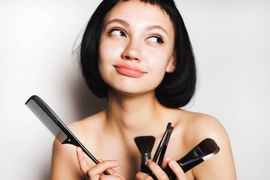  siyah kısa saçlı güzel kız gizemli bir şekilde uzak görünüyor ve onun ellerini makyaj fırça ve tarak tutar