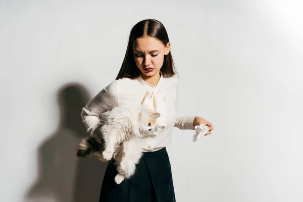 Uma bela jovem comemora parecendo descontente porque ela está segurando um gato, mas ela é alérgica a animais — Fotografia de Stock
