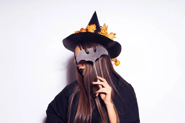 A young sexy gothic girl celebrates halloween, in a black hat, adorned with yellow leaves, covers her face with hair and a drawing of a bat — Stock Photo, Image