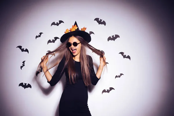 Joven chica gótica sexy celebra halloween, en un sombrero negro, adornado con hojas amarillas y risas —  Fotos de Stock