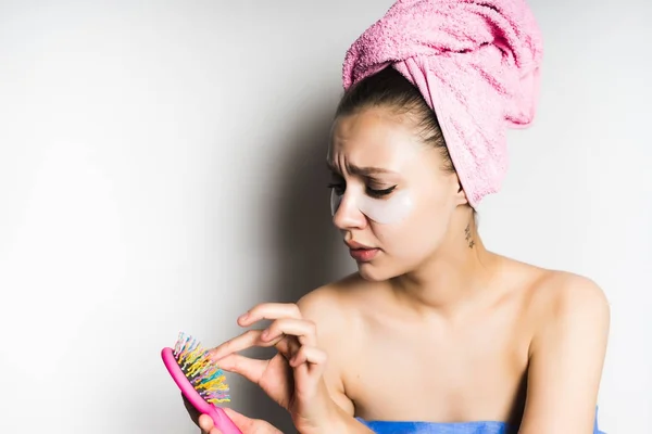 Η κοπέλα μετά από ένα ντους με μια ροζ πετσέτα στο κεφάλι της αφαιρεί τα μαλλιά από ένα όμορφο πολύχρωμο χτένα — Φωτογραφία Αρχείου