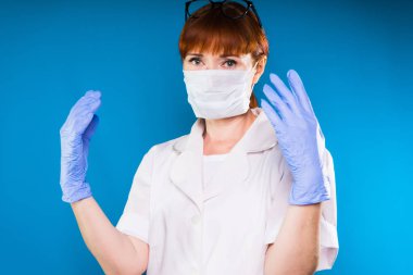 Beyaz tıbbi soyunma elbise, Kızıl saçlı kadın eldivenler ve yordamı önce maske takıyor. Kız doğrudan kameraya bakıyor