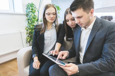 genç bir adam ve iki kızı tablet vasıl arıyorum. Takım elbiseli bir adam bir tablet elinde tutar ve kızlar üzerinde çalışmak için bir şeyler gösteriyor. ofiste