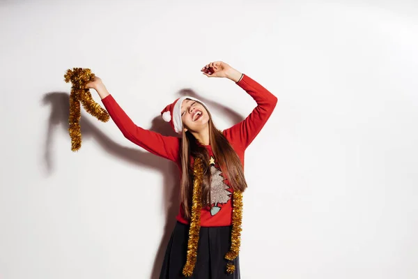 Una giovane ragazza sexy divertente celebra il nuovo anno e il Natale, con un berretto rosso e un maglione alla moda con fili di lame d'oro — Foto Stock