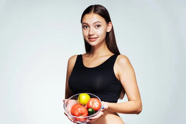 Uma jovem assiste sua figura, quer perder peso, segura um prato com vegetais úteis e frutas em suas mãos — Fotografia de Stock