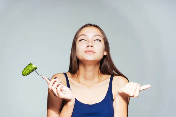 Une jeune fille regarde sa silhouette, veut perdre du poids et mange un concombre faible en calories — Photo