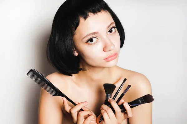 Menina com cabelo preto curto está segurando uma escova para maquiagem e pente — Fotografia de Stock