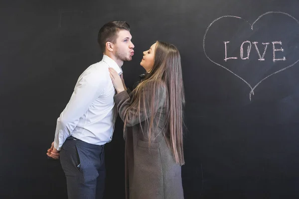 Un jeune homme veut embrasser une fille aux cheveux longs en manteau. sur le tableau, le cœur est sculpté et il est écrit "amour " — Photo