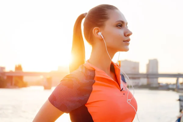 Flickan i sportkläder gick springa på banvallen vid solnedgången. En flicka som lyssnar på musik på en körning — Stockfoto