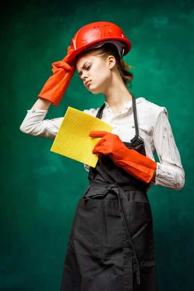 A rapariga vai fazer a limpeza. uma menina em um grande avental preto, luvas de laranja e um pano amarelo em sua mão — Fotografia de Stock