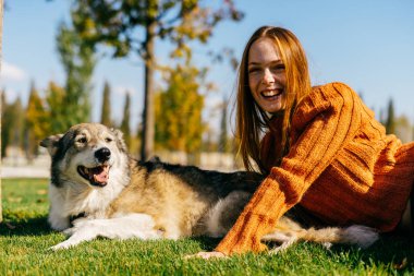 Genç şirin Kızıl saçlı kız ile yeşil çimenlerin üzerinde oturan parkta onun köpek yürüyüş