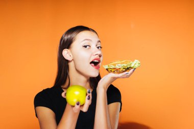 güzel kız, kilo vermek istiyor bir genç tutan yararlı bir elma ve zararlı yüksek kalorili hamburger