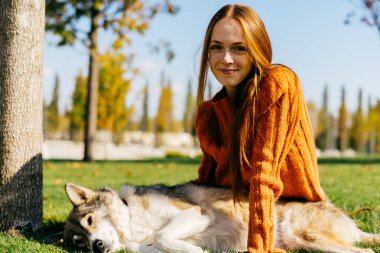 Genç şirin Kızıl saçlı kız parkta yeşil çimenlerin üzerine oturmuş onu köpek ile yürüyüş