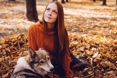 Genç şirin Kızıl saçlı kız köpeğini düşen sonbahar yaprakları bir yığın içinde oturan parkta ile yürüyüş