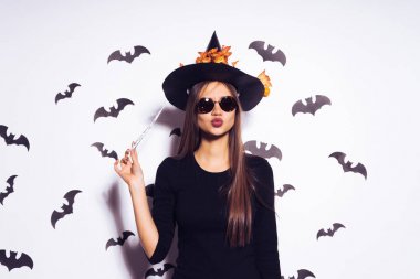 seksi, genç bir Gotik kadın bir cadı, sarı yaprakları ile süslenmiş büyük siyah bir şapka, güneş gözlüğü, holding sihirli bir değnek takıyor Cadılar Bayramı olarak şeklinde