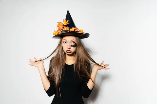 Una joven mujer gótica sexy en forma de bruja en Halloween, en un gran sombrero negro, adornado con hojas amarillas, se ve triste —  Fotos de Stock