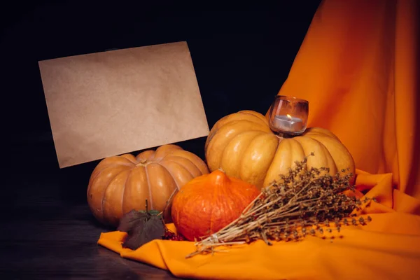 Композиция для украшения дома на Хэллоуин, лежат желтые и оранжевые тыквы, горящие свечи, оранжевая ткань — стоковое фото