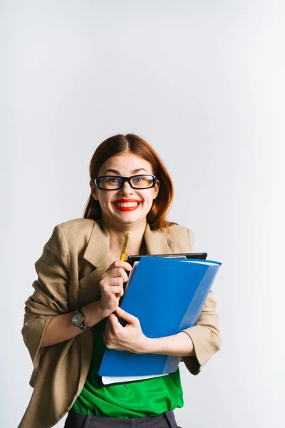 Lachendes rothaariges Mädchen mit Brille hält ein Bündel Ordner und einen Bleistift in der Hand und blickt in die Kamera — Stockfoto