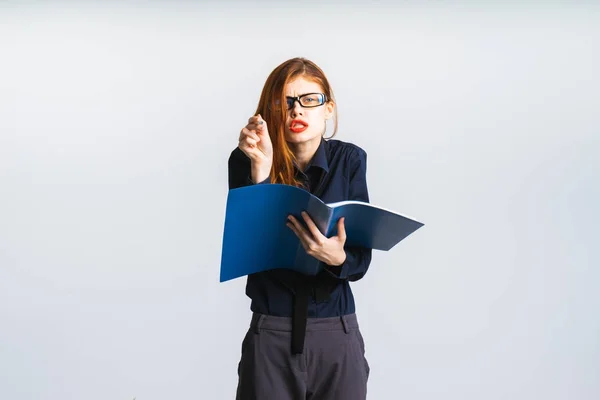 Ein müdes Mädchen mit Brille hält eine offene blaue Mappe in der Hand und will dort etwas aufschreiben — Stockfoto