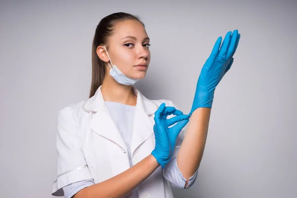Ragazza in vestaglia medica bianca si mette i guanti e si prepara a fare le procedure — Foto Stock