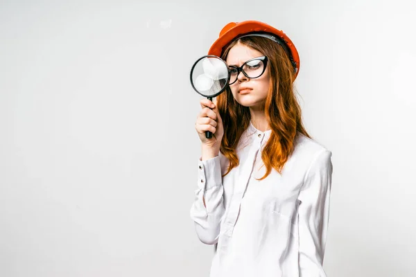 Девушка в очках и в оранжевой шляпе смотрит в увеличительное стекло, изолированные — стоковое фото