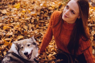 genç güzel kızıl saçlı kız onu köpek parkında sonbahar düşmüş yaprak yığını ile yürüyor