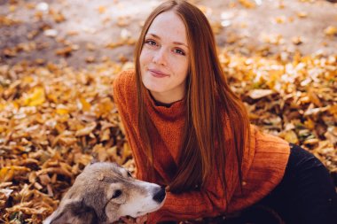 genç güzel kızıl saçlı kız onu köpek parkında sonbahar düşmüş yaprak yığını ile yürüyor